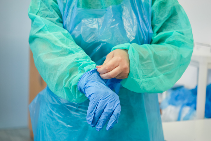 A medical professional's hands in a green gown carefully pull on a blue latex glove, emphasizing important personal safety and hygiene